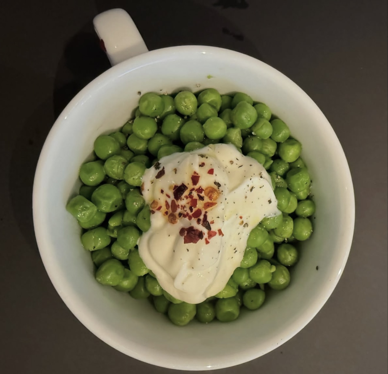 A bowl of green peas with yoghurt, chilli flakes and cracked pepper